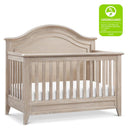 Rustic 4-in-1 convertible crib in sandbar finish, featuring a curved top, slatted sides, and a GREENGUARD Gold certification.