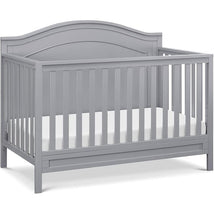 Gray Million Dollar Baby Charlie 4-In-1 Convertible Crib with slatted sides and a curved headboard, featuring a mattress support.
