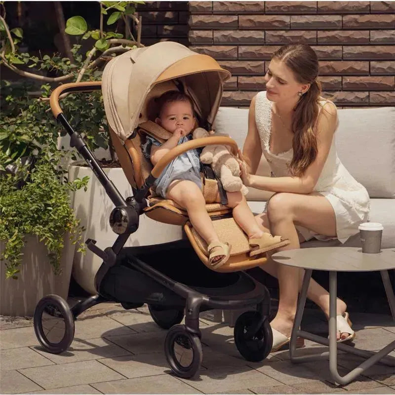 Mima Creo Single Stroller in Mocha Cream with a baby sitting inside, while a woman gently interacts with the child outdoors.
