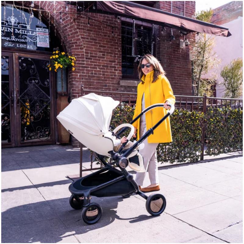 Woman in a yellow coat pushing a Mima Creo Single Stroller in white along a city sidewalk.
