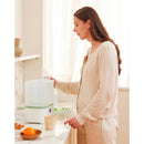 Momcozy 8-in-1 Baby Bottle Steam Sterilizer on a countertop, with a woman loading it with baby bottles.
