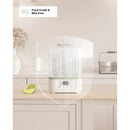 Momcozy 8-in-1 Baby Bottle Steam Sterilizer with digital display, food grade, BPA-free, on a kitchen countertop, beside a lime.
