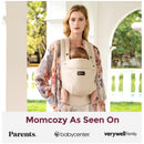 Light amber Momcozy baby carrier worn by a woman with a child inside, outdoors, featuring logos from various parenting brands.