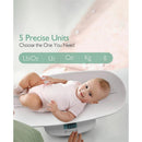 Multi-function baby scale by Momcozy with a baby lying on it, displaying weight options: Lb:Oz, Lb, Oz, Kg, g.