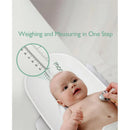 Multi-function baby scale by Momcozy, weighing and measuring a baby, with a measuring tape and a stethoscope visible.