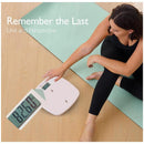 Multi-function baby scale displaying weight of 82.6 kg, with a woman seated beside it on a yoga mat.