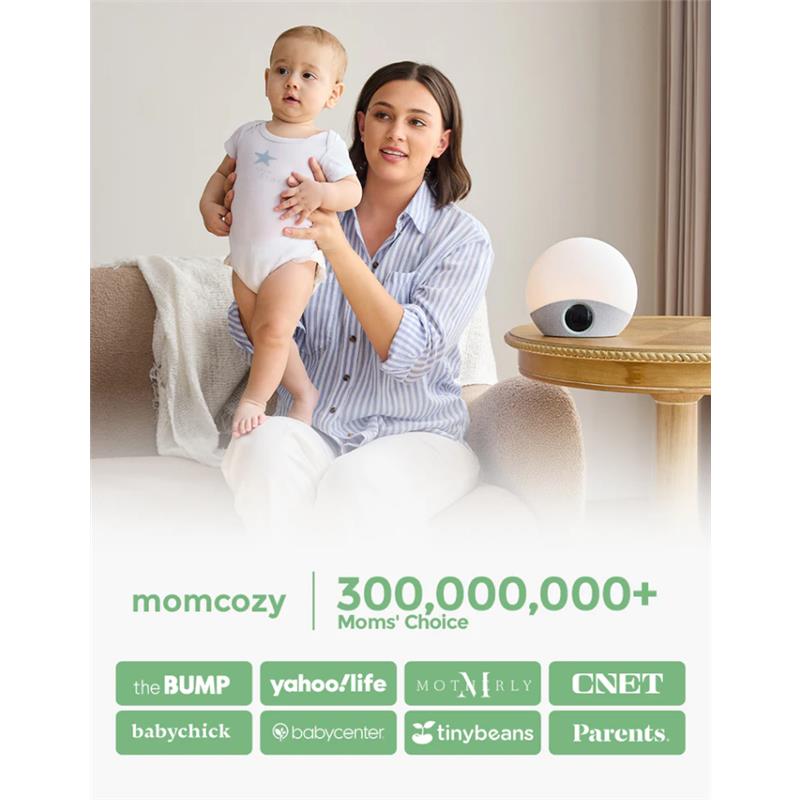 A woman holds a baby while sitting beside the Momcozy Sunrise Alarm Clock, which emits soft light.