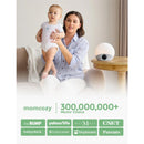 A woman holds a baby while sitting beside the Momcozy Sunrise Alarm Clock, which emits soft light.
