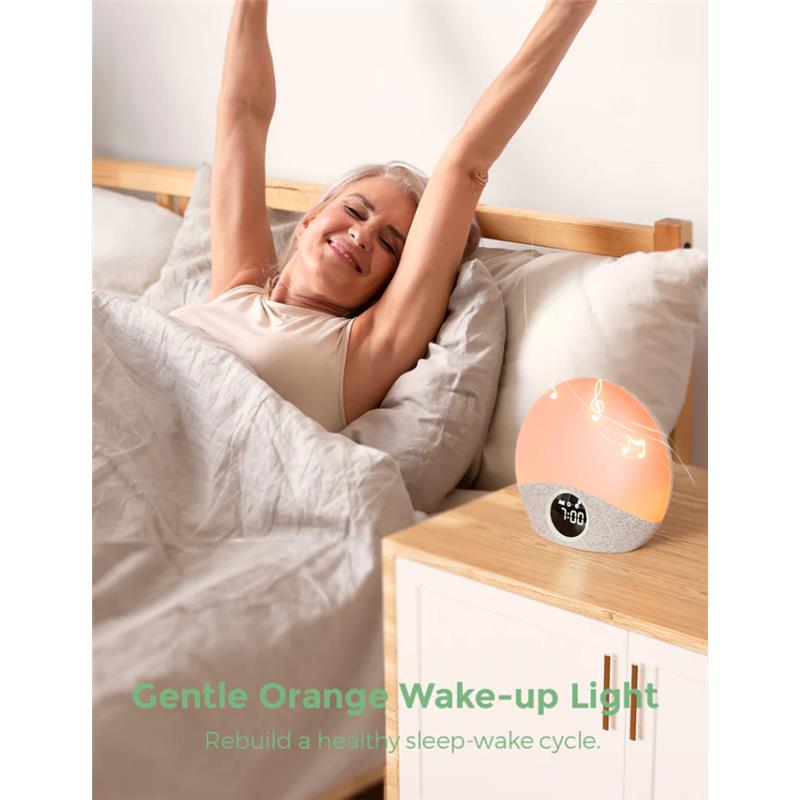 Woman stretching in bed next to the Momcozy Sunrise Alarm Clock, which displays time and emits a gentle orange light.