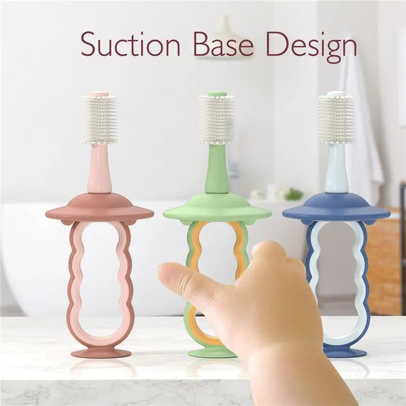 Momcozy toothbrushes in pink, green, and blue with suction bases, designed for children, with a hand reaching towards them.