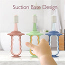 Momcozy toothbrushes in pink, green, and blue with suction bases, designed for children, with a hand reaching towards them.