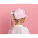 Pink embroidered cap with a white bow, worn by a child, against a pink background.