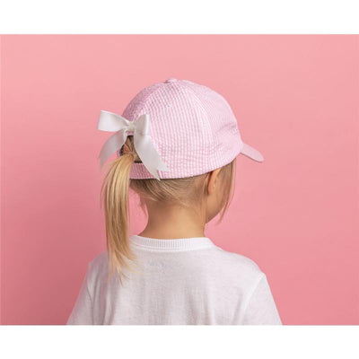 Pink embroidered cap with a white bow, worn by a child, against a pink background.