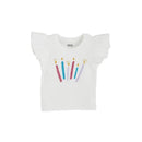 White birthday tee with ruffled sleeves featuring colorful candle designs and gold flame details.
