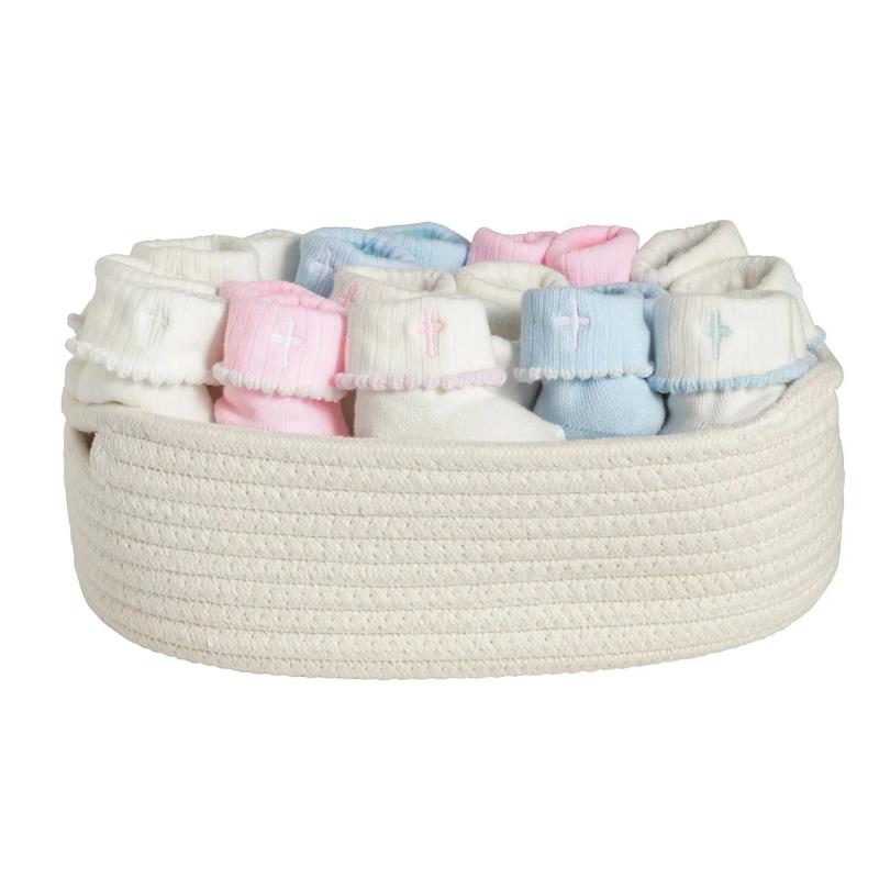 Pink and white cross-themed socks for infants, neatly arranged in a round woven basket.