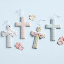 Ceramic crosses in pastel colors, featuring floral designs and bows, displayed with decorative flowers on a blue background.