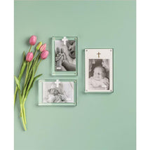 Vertical layered acrylic frames displaying black-and-white baby photos with decorative crosses alongside pink tulips on a green background.