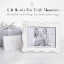 White enamel cross picture frame displaying a black-and-white photo of three smiling children, alongside a gift box and card.