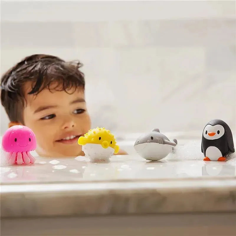 A smiling child in a bath enjoys colorful ocean-themed squirters, including a pink jellyfish, yellow pufferfish, gray dolphin, and black penguin.