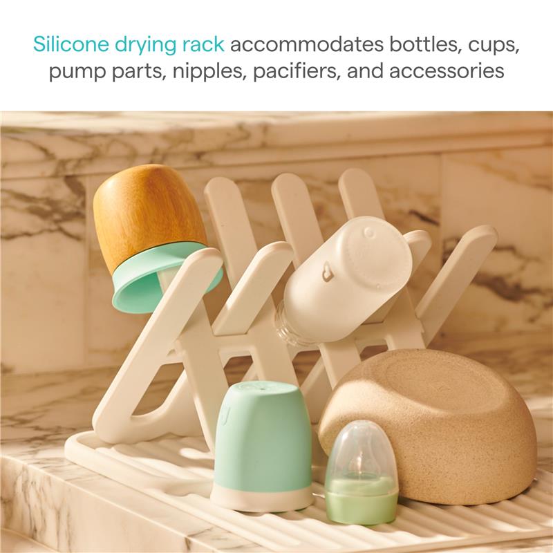 Silicone drying rack in white displaying a variety of colorful baby bottles, cups, and accessories on a marble countertop.