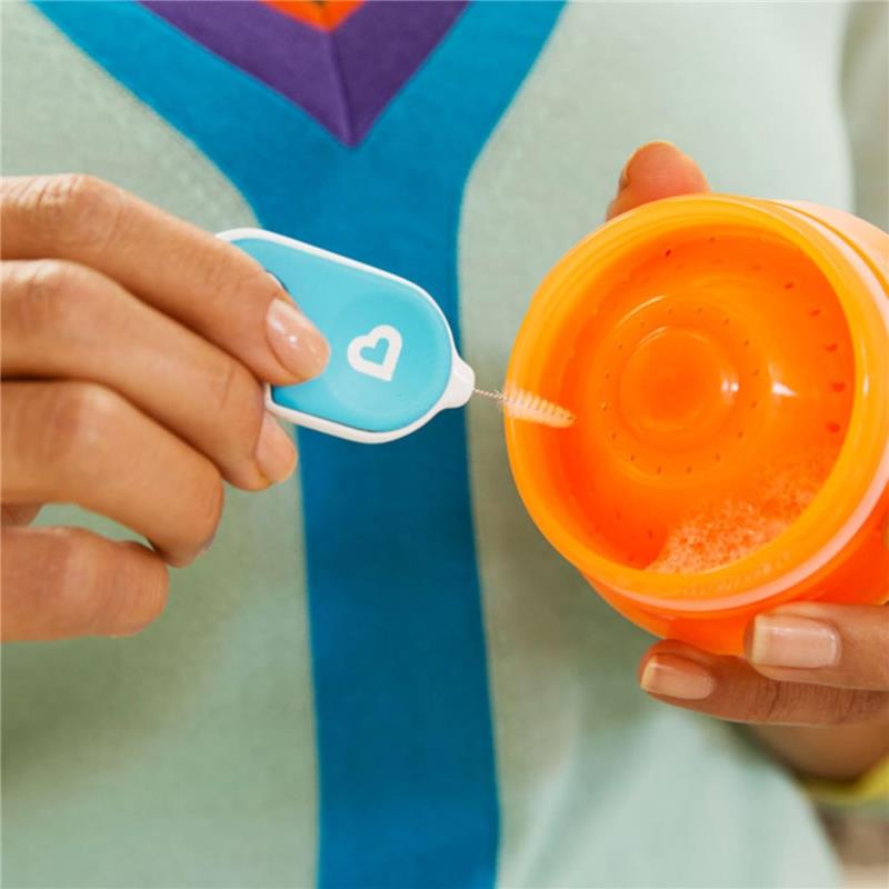 Hand holding a cleaning brush with a heart design, cleaning an orange container filled with suds.