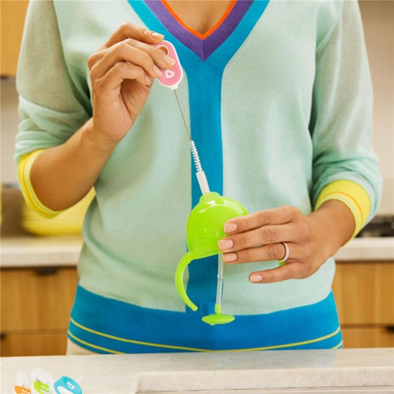 A person using a pink cleaning brush to clean a green Munchkin cup, demonstrating the cleaning process in a kitchen setting.