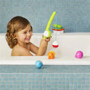 A smiling child holds a green fishing rod in a bathtub, with colorful fish toys floating around and a blue tiled background.