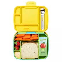 Bento box in green and yellow containing carrots, strawberries, a sandwich, and a juice box, with stainless steel utensils.