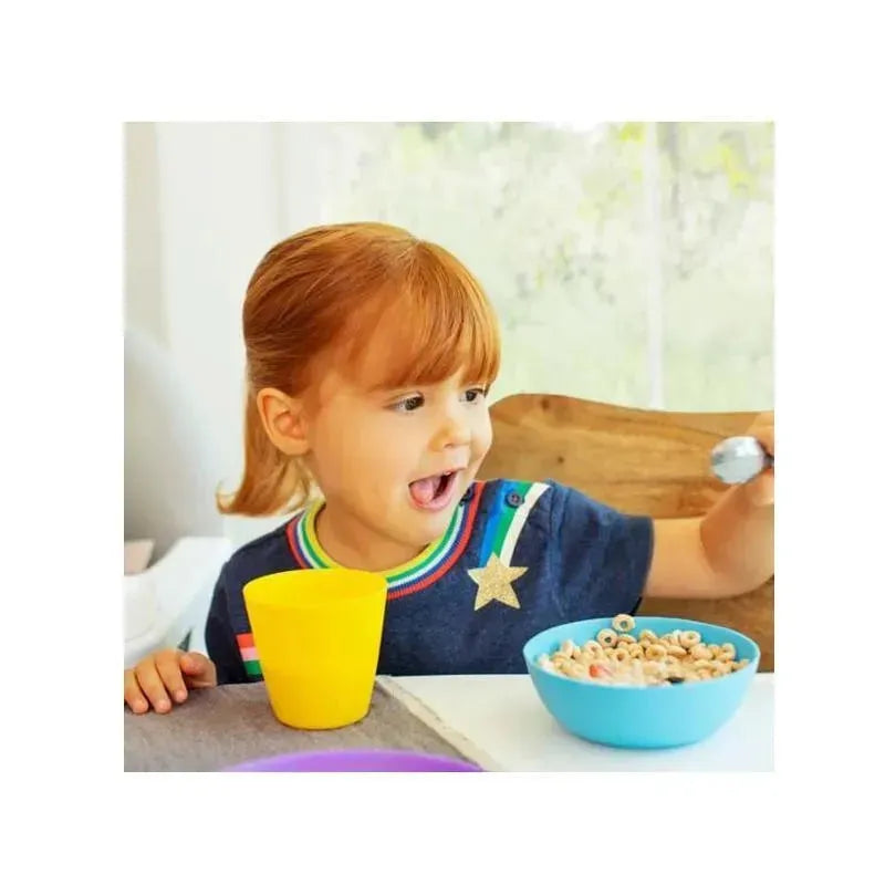 A cheerful child with red hair sits at a table, excitedly eating cereal from a blue bowl, with a yellow cup nearby.
