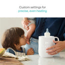 Munchkin Precision Baby Bottle Warmer in white, featuring a digital display and a baby bottle positioned on top, with a parent and child nearby.