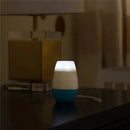 Munchkin Shhh Portable Sleep Machine in white and blue, softly illuminated on a dark surface, with control buttons visible.