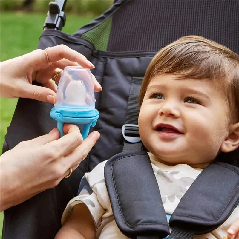 Silicone baby food feeder held by an adult, with a smiling baby in a high chair, enjoying the feeding process.