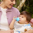 Baby enjoying a blue Munchkin silicone food feeder while sitting with an adult outdoors.