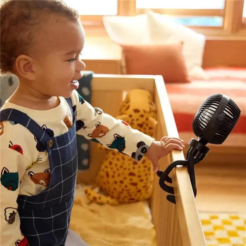 A toddler smiles while reaching for a Munchkin stroller fan, featuring a portable design and black clip attachment.