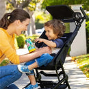 A mother smiles at her young child in a stroller, which has a portable Munchkin fan, while the child holds a colorful cup.