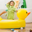 Child in a green bathrobe plays with a toy while standing by a yellow inflatable duck tub, surrounded by colorful bath toys.