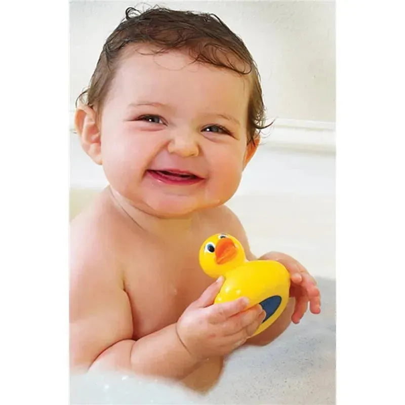 Smiling baby holding a Munchkin White Hot Safety Bath Ducky while sitting in a bathtub filled with water.