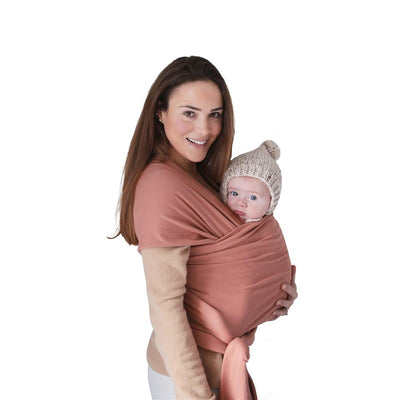 Mushie 100% Organic Cotton Baby Wrap Carrier in Cedar, worn by a woman carrying a baby in a knit hat.