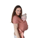 Mushie 100% Organic Cotton Baby Wrap Carrier in Cedar, worn by a woman carrying a baby in a knit hat.