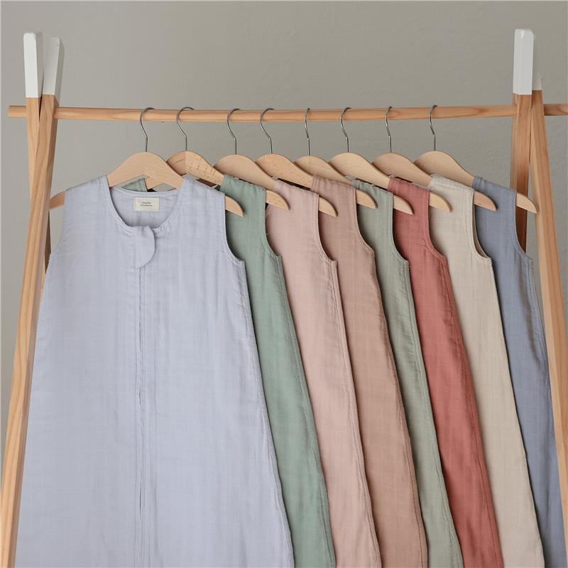 Mushie 100% Organic Cotton Muslin Baby Wearable Blankets displayed on a wooden rack in various soft colors.