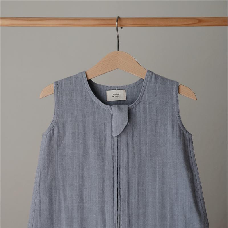 100% organic cotton muslin baby wearable blanket in a soft blue shade hung on a wooden hanger.