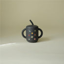 100% silicone training cup for toddlers, featuring a black body with colorful planet designs and a straw.