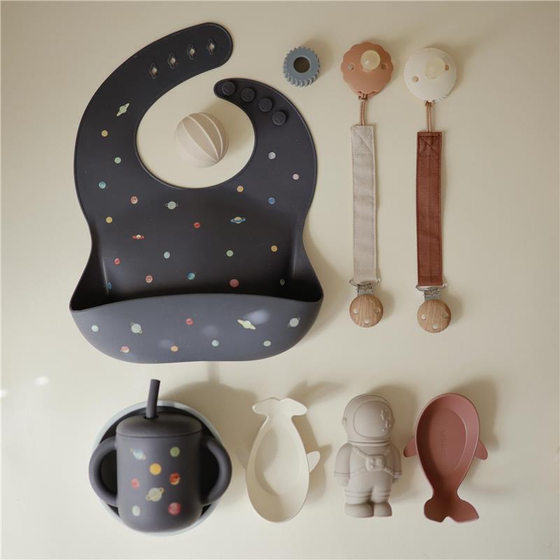 Silicone training cup with straw and colorful planet design, alongside a matching bib and various playful accessories.