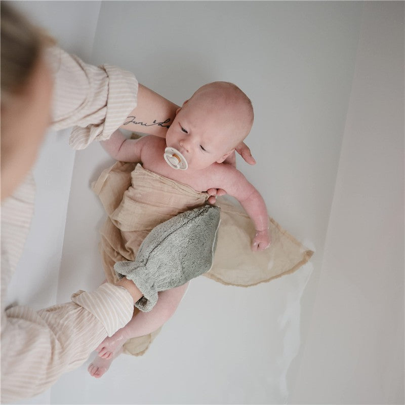 Mushie Organic Cotton Bath Mitt in gray being used to bathe a baby wrapped in a light cloth.