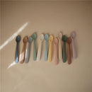 Silicone feeding spoons in various pastel colors, arranged neatly on a light background.