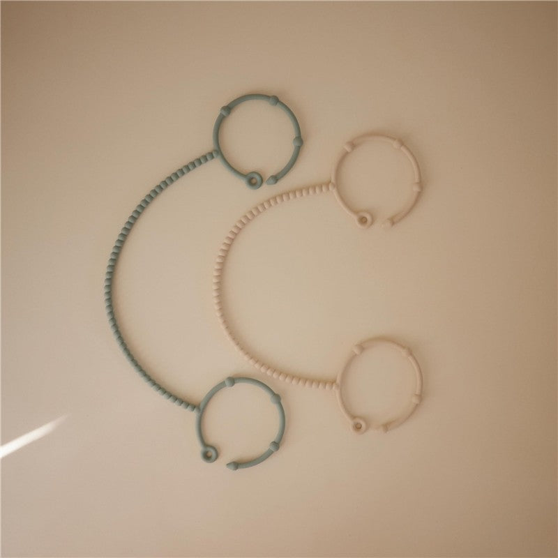 Adjustable silicone straps in Cambridge Blue and Shifting Sand colors, arranged in a playful design on a neutral background.