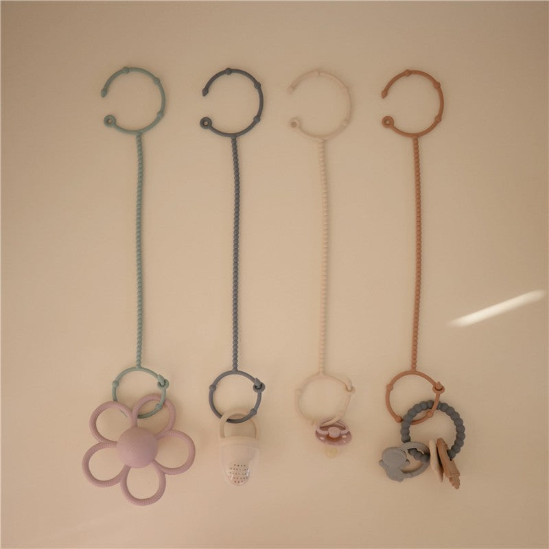 Adjustable silicone strap set in Cambridge Blue and Shifting Sand, featuring a flower, pacifier, and animal-shaped toys.