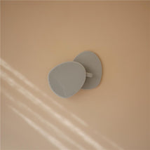 Silicone baby bath cradle cap brush in light gray, featuring a textured surface and handle, resting against a peach background.