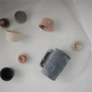 Mushie Bath Rinse Cup in sage color, surrounded by various small rinsing cups, all resting in soapy water.
