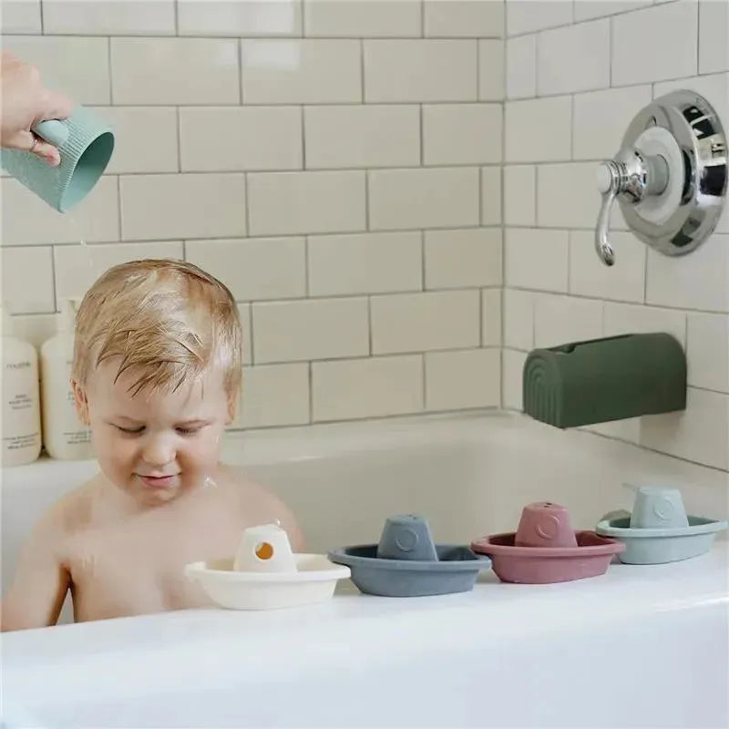 Child enjoying bath time as an adult pours water from a sage-colored rinse cup, with colorful rinse boats nearby.